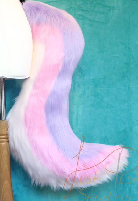A long, 25 inch, luxury faux fur wold tail with stripes running from the base to tip in an 's' type curve. Top colour is lilac, then a pale pink with the underside as white. There are belt loops to hold the tail to a belt, this is designed and made by fish