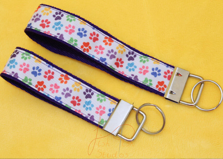 a cute photo showing two colourful paw print themed keyrings made of fabric. one is slightly bigger than the other. Both have little cartoon paw prints on them with a white background. handmade in the UK by fishpish studios