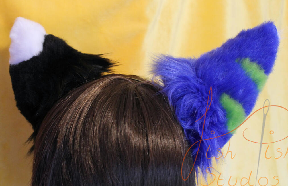 A pair of complex asymmetrical wolf ears commissioned by a client. One is black with a white tip, the other blue with green stripes. Made of luxury faux fur, these are posable on a metal headband. Handmade by fishpish studios in the UK
